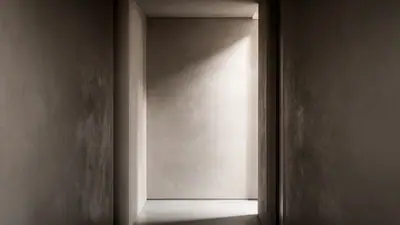 Foto editorial de corredor estreito com revestimento de cimento queimado texturizado, iluminado por luz lateral suave que destaca as variações da superfície.