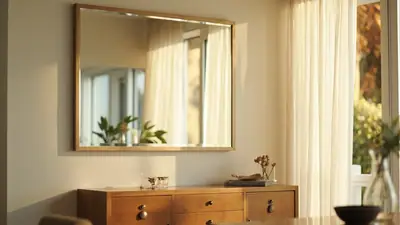 Sala de estar ampla com espelho reto sobre aparador de madeira refletindo janela e luz natural